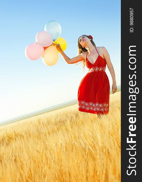 Young woman in a wheat field holding colorful balloons. Young woman in a wheat field holding colorful balloons