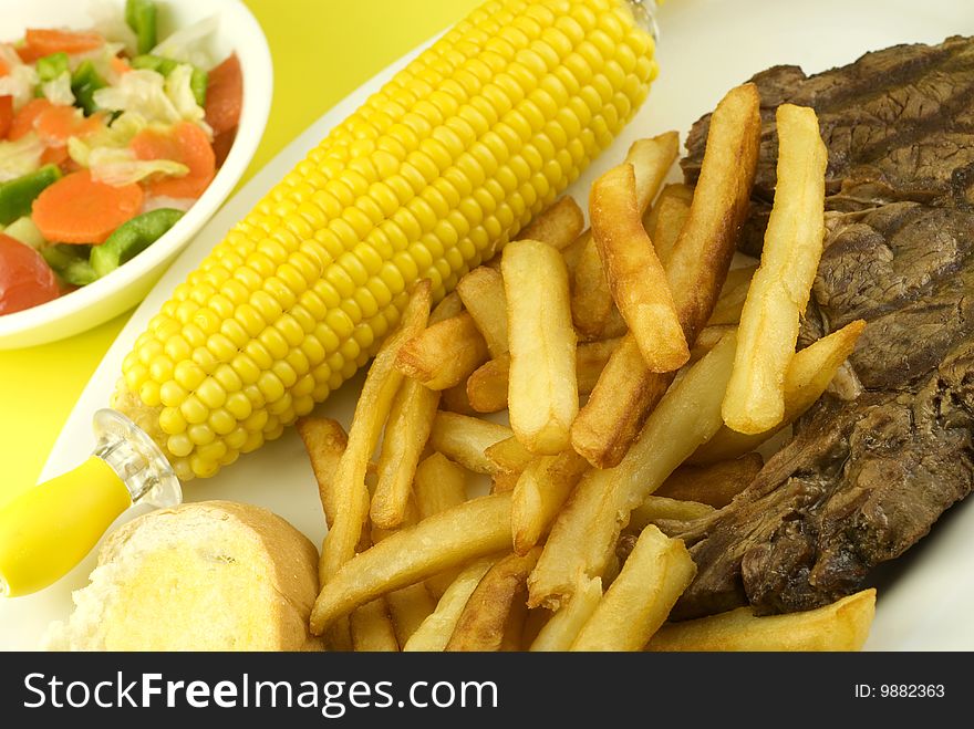 A grilled ribeye steak dinner, with corn on the cob, french fries, toasted french bread, and side salad, horizontal with copy space. A grilled ribeye steak dinner, with corn on the cob, french fries, toasted french bread, and side salad, horizontal with copy space