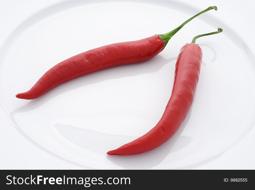 Two red peppers resting on a white plate. Two red peppers resting on a white plate.
