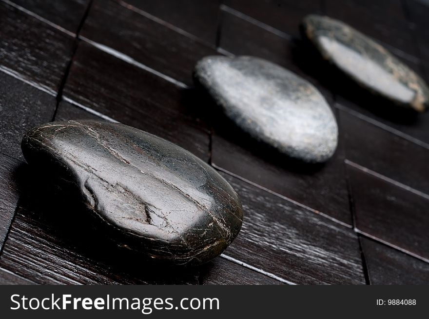 Tilted horizontal shallow focus image of 3 river rocks on black wood