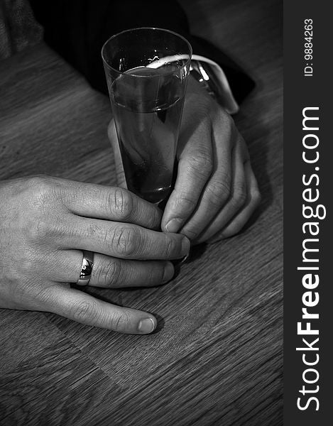 A pair of hands holding a drink glass. A ring on one of the fingers. watch is visable. A pair of hands holding a drink glass. A ring on one of the fingers. watch is visable