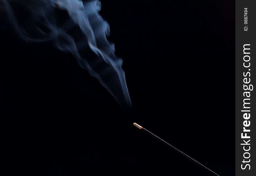 Smouldering aroma stick on a black background. There is a smoke above the stick. Smouldering aroma stick on a black background. There is a smoke above the stick.