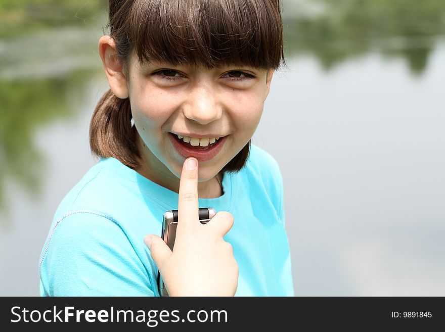 Portrait of nice young smiling girl handing mobile phone on nature background