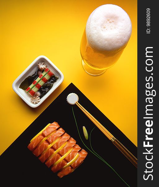 Glass of beer on yellow background with salmon and squid and chopsticks. Glass of beer on yellow background with salmon and squid and chopsticks