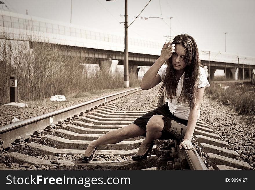 The girl sits on rails near to a motorway. The girl sits on rails near to a motorway