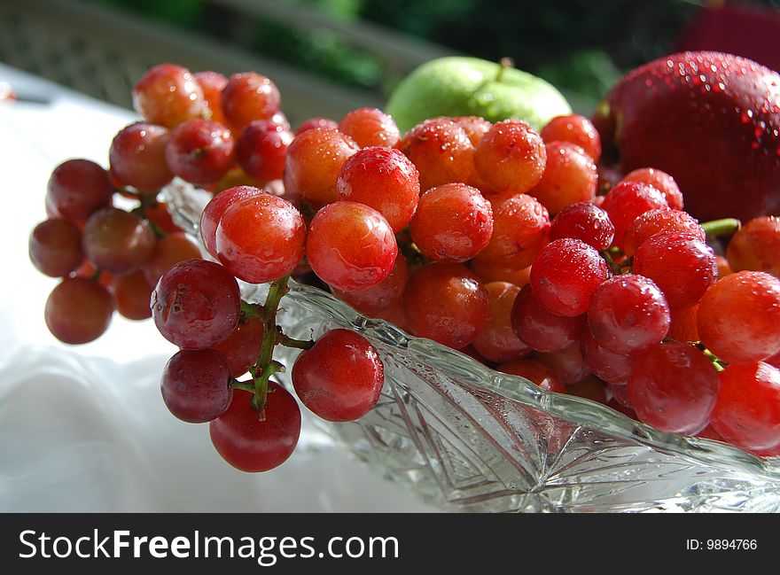 Fresh and juicy grapes in a crystal bowl with red and green apples in the background