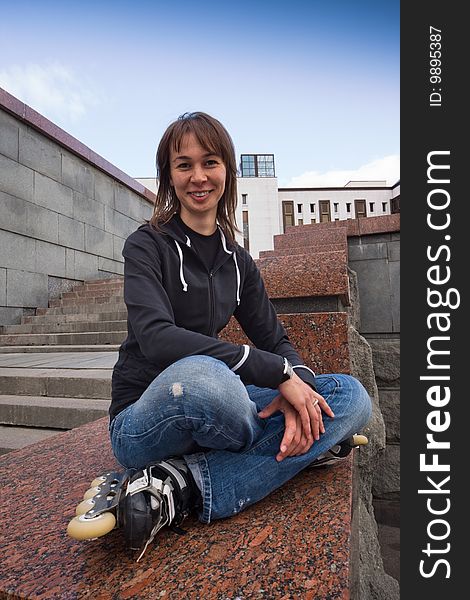 Rollerskating girl in blue jeans sitting on granite plate - wide angle portrait