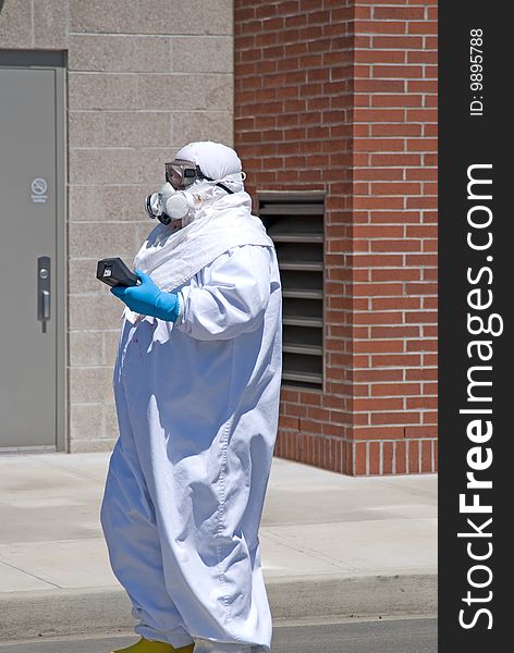 A man walking down a street in the Northwest in a suit designed to keep germs out holding a medical instrument. A man walking down a street in the Northwest in a suit designed to keep germs out holding a medical instrument.