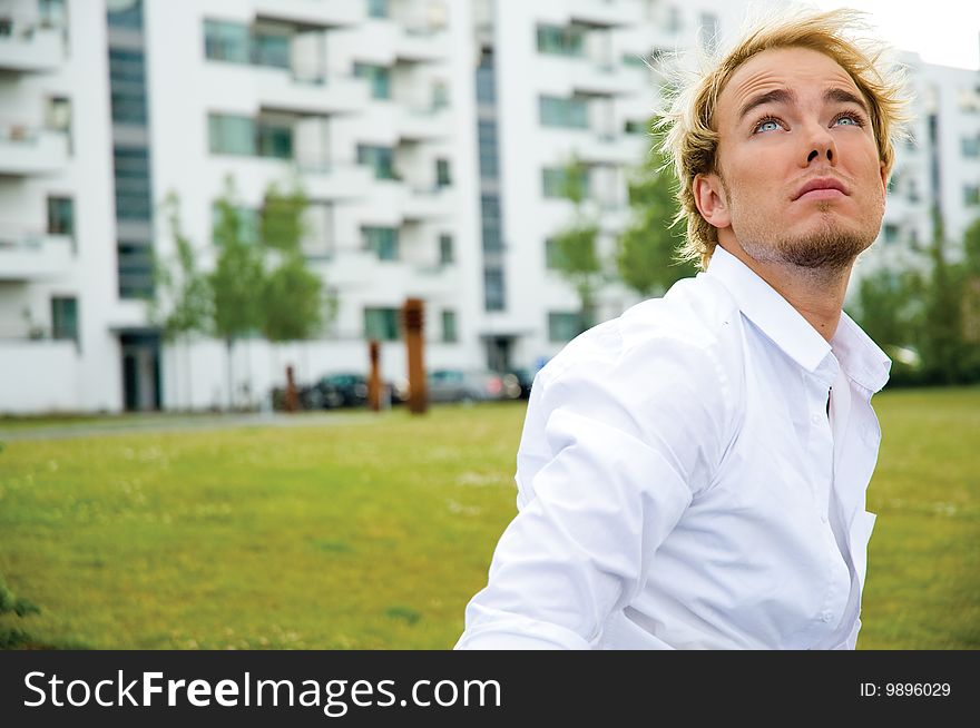 Young man standing on green grass looking at the sky in front of white buildings. Young man standing on green grass looking at the sky in front of white buildings