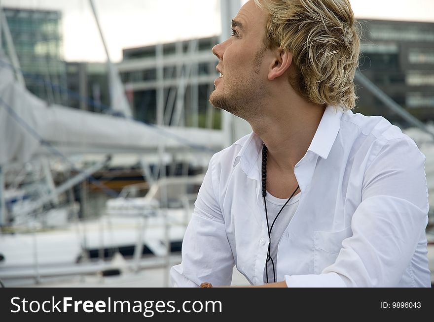 Young man sitting near some yachts at a yachtclub. Young man sitting near some yachts at a yachtclub