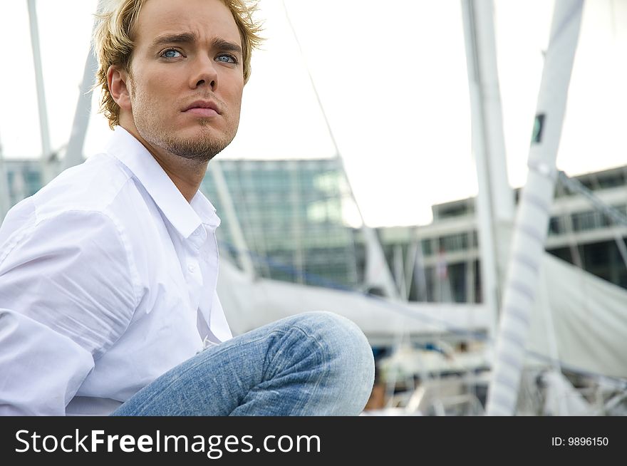 Young man sitting near some yachts at a yachtclub. Young man sitting near some yachts at a yachtclub