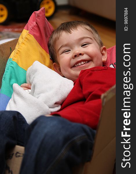 A young boy sitting in a box and smiling while holding his blanket. A young boy sitting in a box and smiling while holding his blanket.