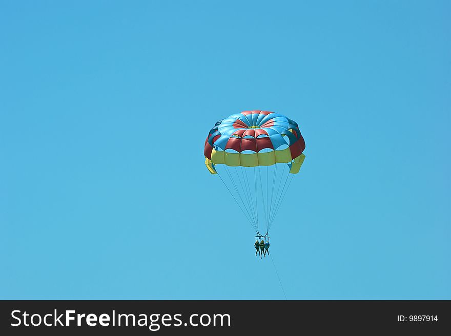 A colorful parasail in the sky with three passengers. A colorful parasail in the sky with three passengers.