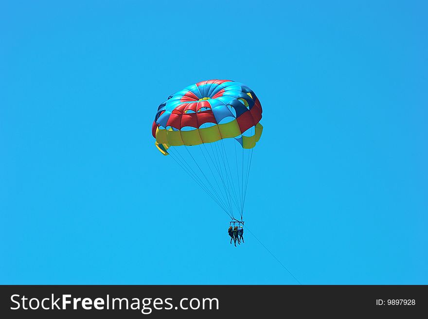 A multicolored parasail at an angle with three passengers. A multicolored parasail at an angle with three passengers.