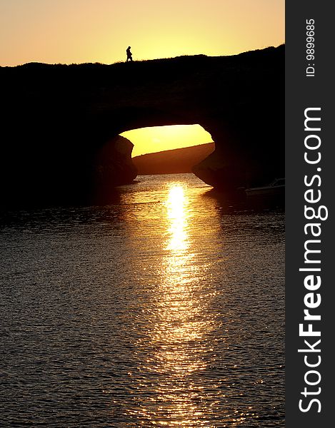 Sunset over the sea on mediterranean island, somebody is walking over a rocky arch. Sunset over the sea on mediterranean island, somebody is walking over a rocky arch