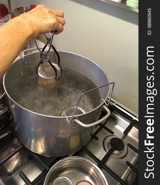 Lowering filled jam jars into boiling water bath canner