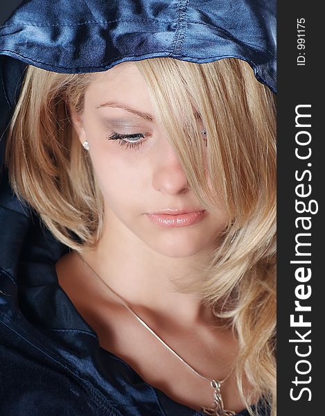 Blonde girl looking down with a dark blue blouse and a hood on his head, close-up