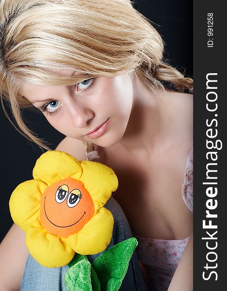 Beautiful country girl in light pink blouse and blue jeans with a flower toy, smiling. Beautiful country girl in light pink blouse and blue jeans with a flower toy, smiling