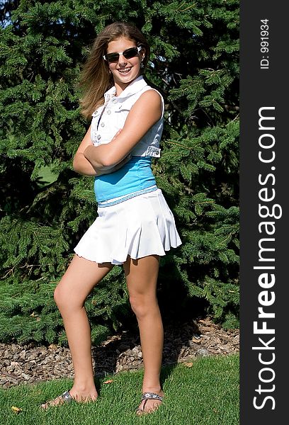 Pretty teenage girl in sunglasses and skirt striking a pose in front of pine trees. Pretty teenage girl in sunglasses and skirt striking a pose in front of pine trees