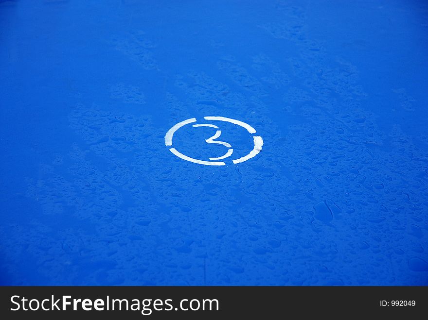 Figure of three in a white circle on a dark blue wet surface. Figure of three in a white circle on a dark blue wet surface