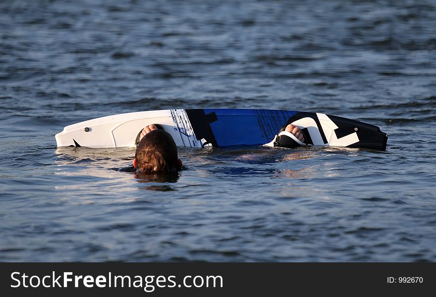 A water ski boarder fallen in with his head and edge of board showing. A water ski boarder fallen in with his head and edge of board showing