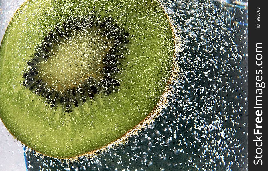 Slice of kiwi fruit diving through splash of bubbles. Slice of kiwi fruit diving through splash of bubbles.