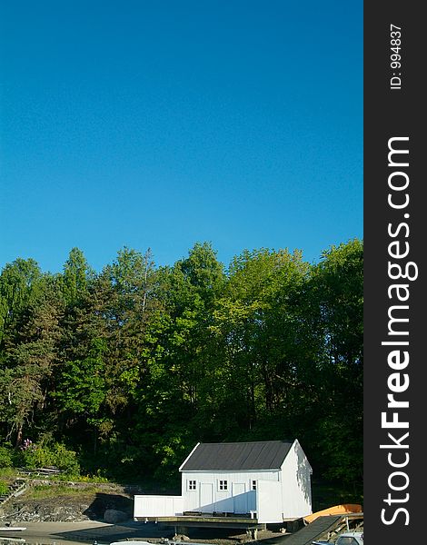 White boathouse, green forest and blue sky