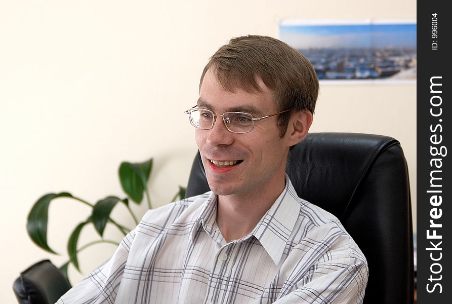 Businessman sits in armchair with a smile, office plants at background. Businessman sits in armchair with a smile, office plants at background