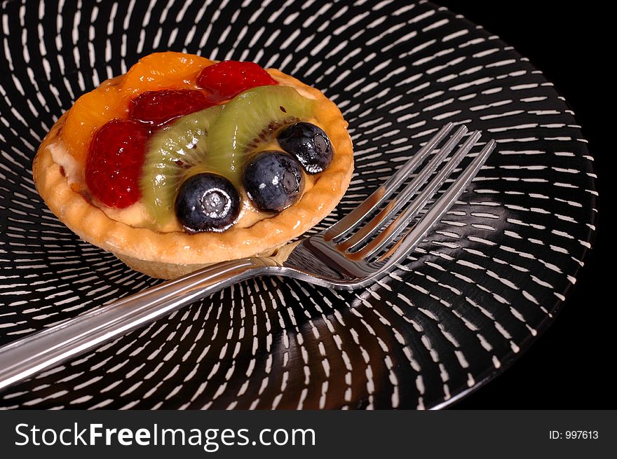 Fruit tart on black and white plate with fork