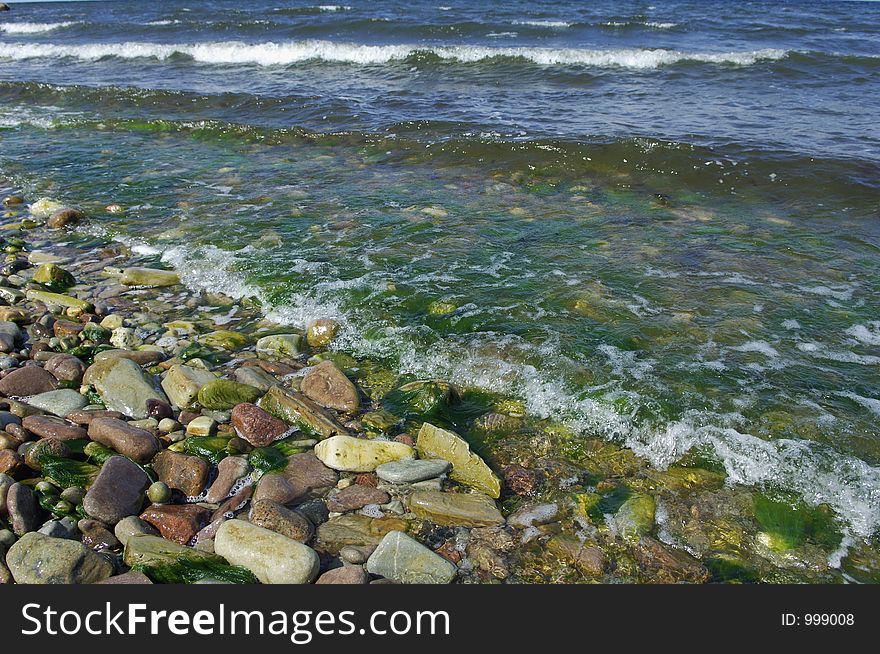 Rocks, pebbles and seaweed being washed over by little waves from sea. Rocks, pebbles and seaweed being washed over by little waves from sea