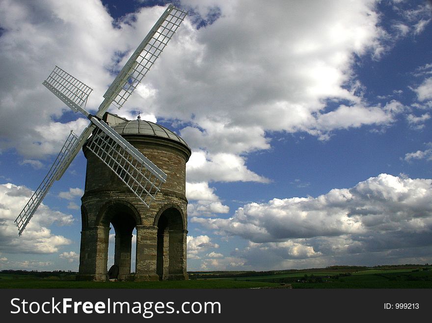 Stone windmill on stilts against clouds and blue sky