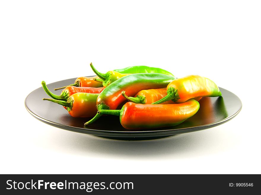 Red and green chillis on a black plate with clipping path on a white background