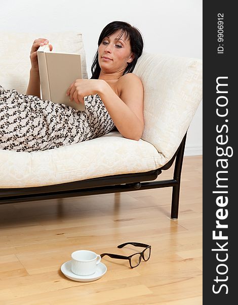 Leisure activity woman lying on couch on wooden floor with glasses and cup relaxing while reading book