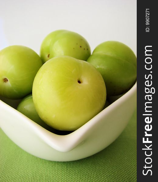 Green plums in a white bowl