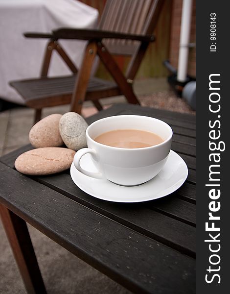 Outdoor cup of tea in a white cup and saucer with stones on a wooden background