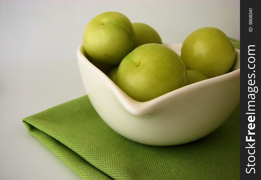 Green plums in a white bowl