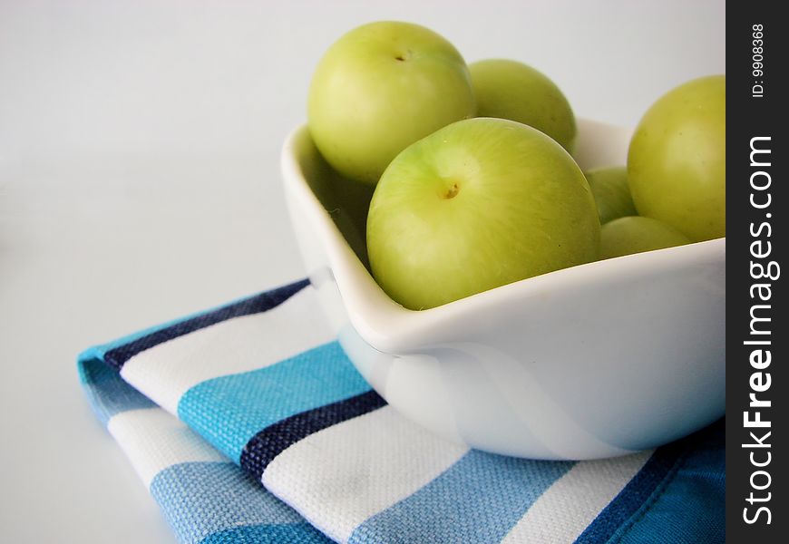 Green plums in a white bowl