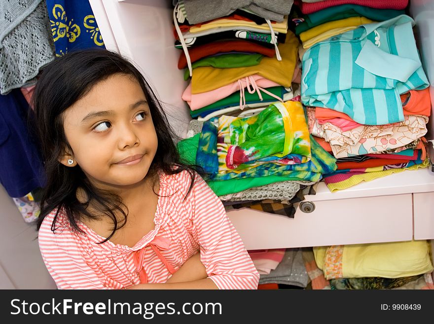 Children lifestyle concept: sweet asian little girl seems to have some thought of her clothing collection in the clothes closet. Children lifestyle concept: sweet asian little girl seems to have some thought of her clothing collection in the clothes closet