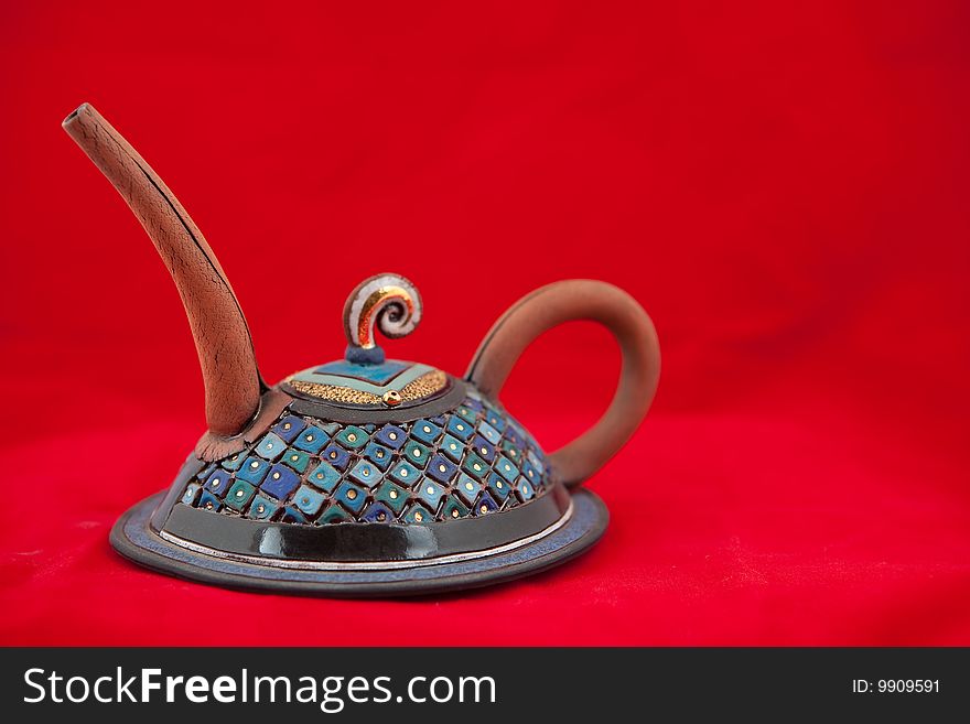 Solitary clay hand crafted very ornate teapot on red background. Solitary clay hand crafted very ornate teapot on red background