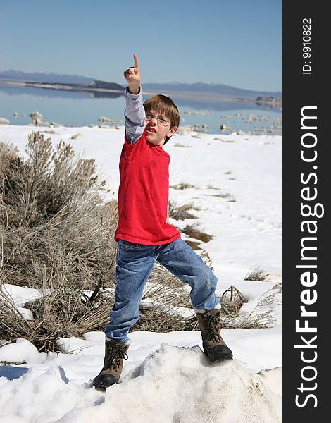 Boy standing on a rock in front of a lake in the snow pointing up. Boy standing on a rock in front of a lake in the snow pointing up