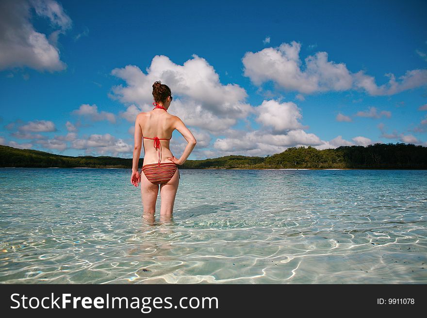 A young woman standing in the water of a beautiful ocean with clouds overhead. A young woman standing in the water of a beautiful ocean with clouds overhead