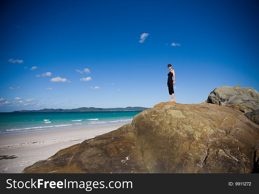 A young woman stands atop big rocks near the oceans edge. A young woman stands atop big rocks near the oceans edge