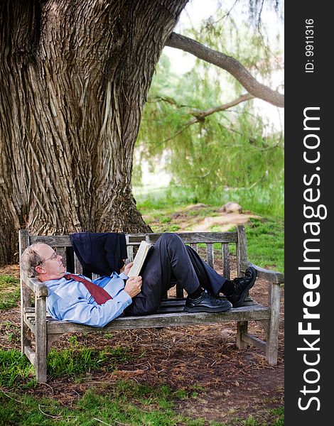 Older man reads while relaxing on a park bench. Older man reads while relaxing on a park bench