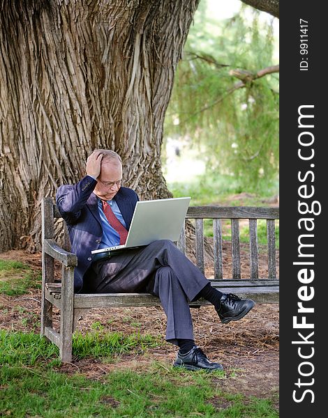 An older man becomes frustrated while using his laptop computer in the park. An older man becomes frustrated while using his laptop computer in the park