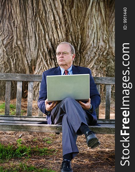 An older business man looks into the distance while working on his laptop computer. An older business man looks into the distance while working on his laptop computer