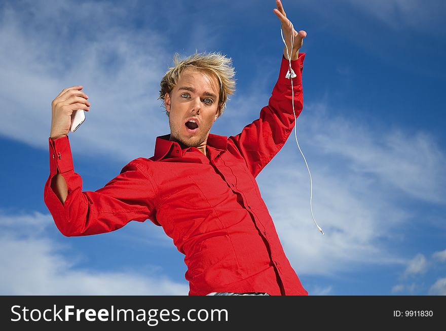 Young man holding a mobilephone in one hand, earphones in the other, wearing a red shirt. Young man holding a mobilephone in one hand, earphones in the other, wearing a red shirt