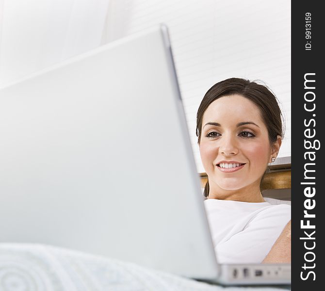 A beautiful young woman is sitting in a room and working on a laptop.  She is smiling and is looking at the screen.  Square framed shot. A beautiful young woman is sitting in a room and working on a laptop.  She is smiling and is looking at the screen.  Square framed shot.