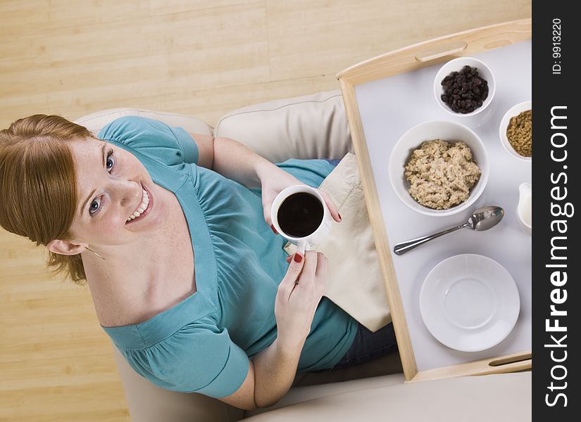 A cute redheaded woman eating breakfast from a tray. She is looking up at the camera and is smiling. Horizontally framed shot. A cute redheaded woman eating breakfast from a tray. She is looking up at the camera and is smiling. Horizontally framed shot.