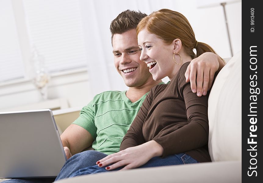 A young and attractive couple sitting together and viewing a laptop screen. They are smiling and laughing. Horizontally framed photo. A young and attractive couple sitting together and viewing a laptop screen. They are smiling and laughing. Horizontally framed photo.