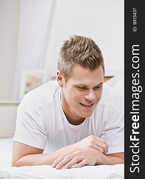 An attractive young man relaxing on a bed.  He is smiling and is looking away from the camera. Vertically framed photo. An attractive young man relaxing on a bed.  He is smiling and is looking away from the camera. Vertically framed photo.